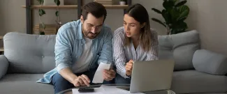 A couple sitting on a couch working on a laptop together.