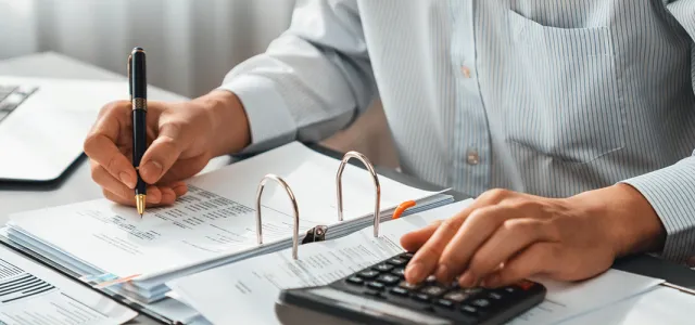 A person at a desk, using a calculator and writing in a notebook.